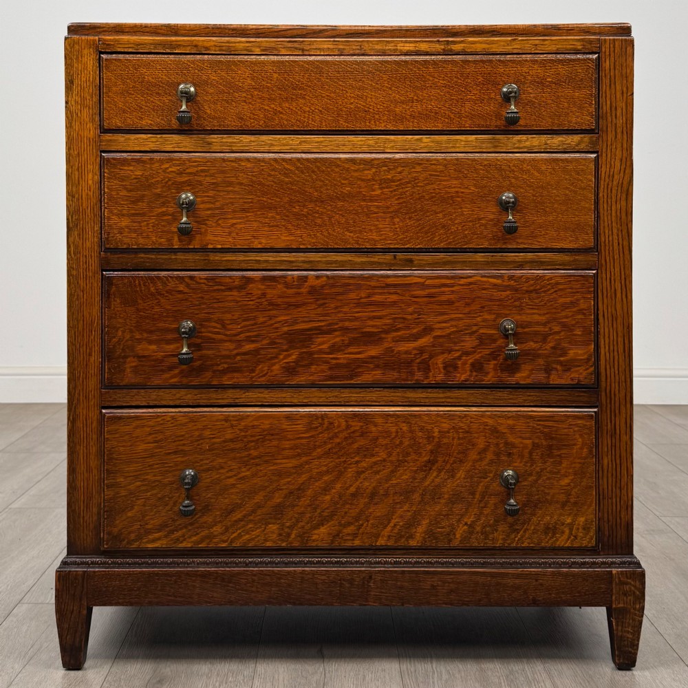 An antique Edwardian oak chest featuring four full-width drawers with brass teardrop handles and tapered legs.
