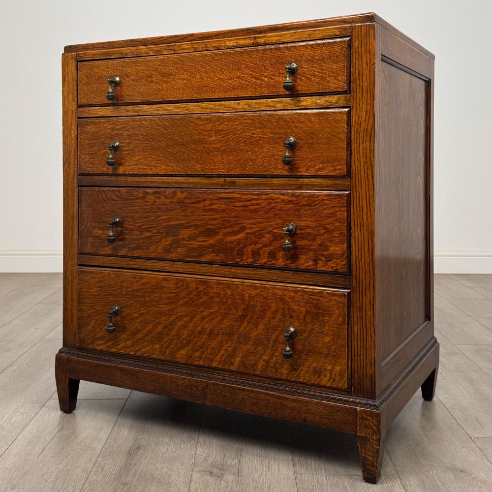 An antique Edwardian oak chest featuring four full-width drawers with brass teardrop handles and tapered legs. View II