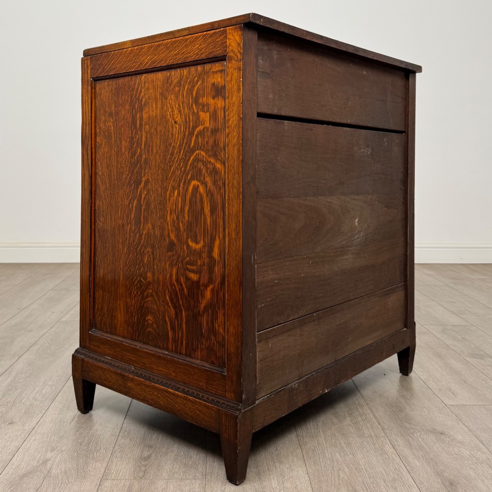 An antique Edwardian oak chest featuring four full-width drawers with brass teardrop handles and tapered legs. View IV