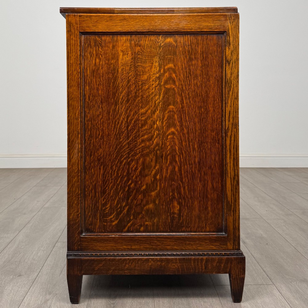 An antique Edwardian oak chest featuring four full-width drawers with brass teardrop handles and tapered legs. View VII