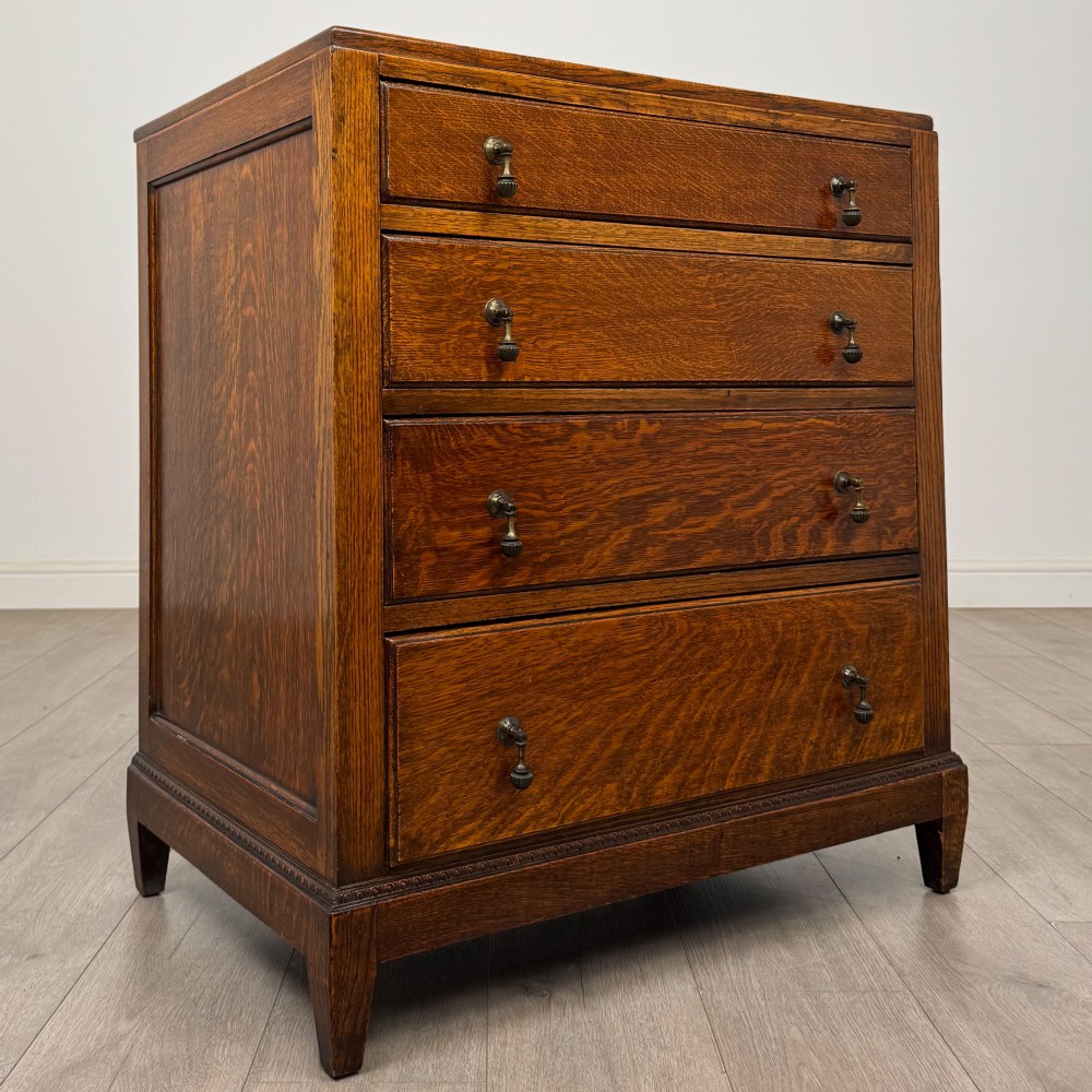 An antique Edwardian oak chest featuring four full-width drawers with brass teardrop handles and tapered legs. View VIII