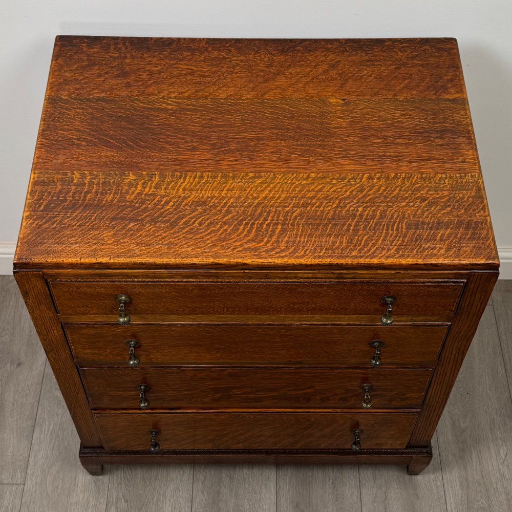 An antique Edwardian oak chest featuring four full-width drawers with brass teardrop handles and tapered legs. View IX