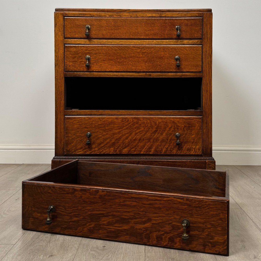 An antique Edwardian oak chest featuring four full-width drawers with brass teardrop handles and tapered legs. View X