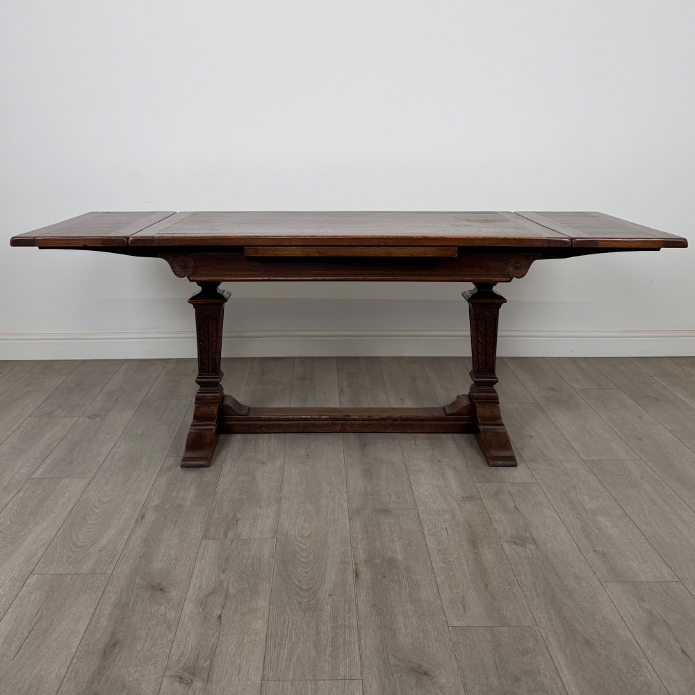 A dark oak draw leaf dining table featuring two extendable leaves, carved pedestal supports, and a low connecting stretcher base. View II