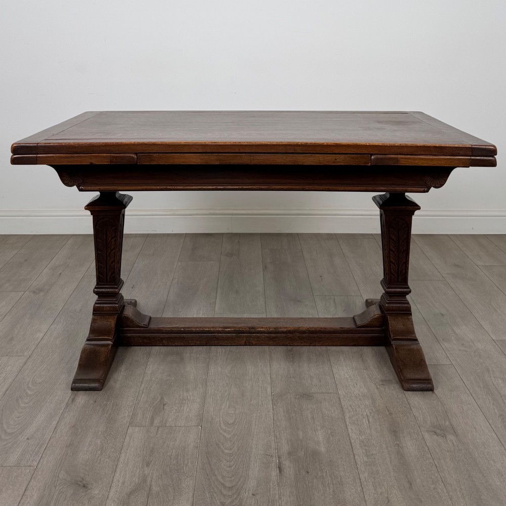 A dark oak draw leaf dining table featuring two extendable leaves, carved pedestal supports, and a low connecting stretcher base. View III