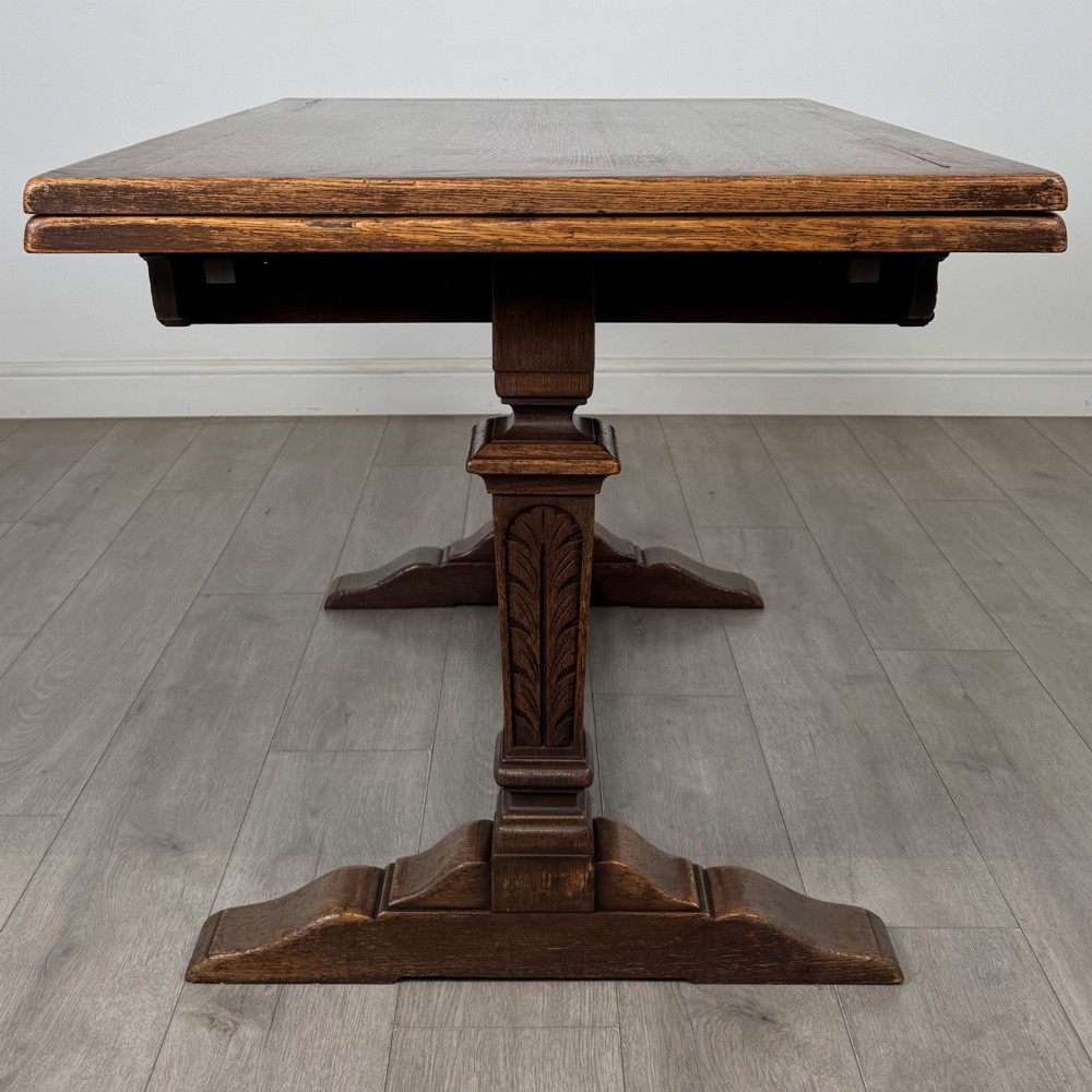 A dark oak draw leaf dining table featuring two extendable leaves, carved pedestal supports, and a low connecting stretcher base. View IV