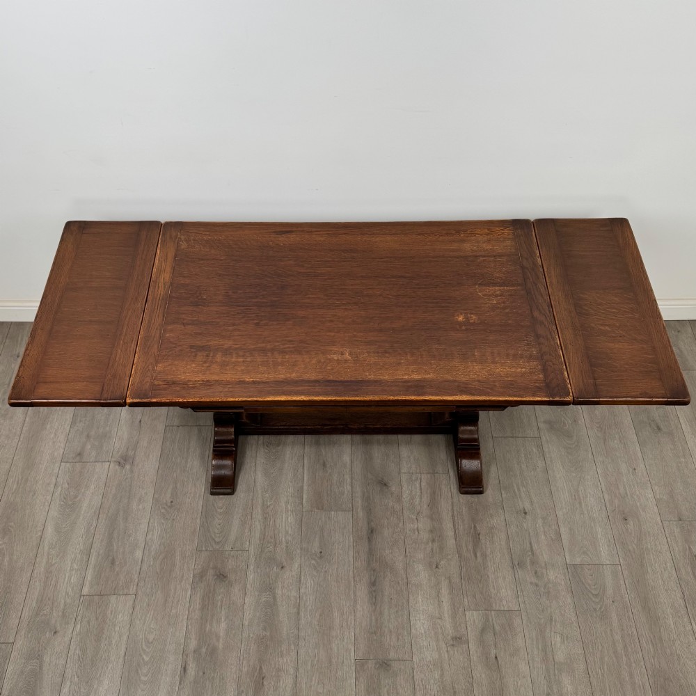 A dark oak draw leaf dining table featuring two extendable leaves, carved pedestal supports, and a low connecting stretcher base. View V