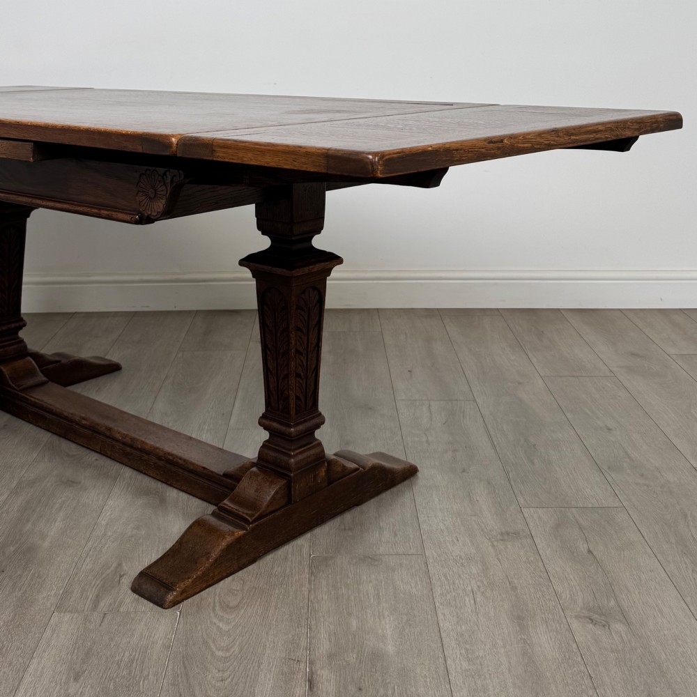 A dark oak draw leaf dining table featuring two extendable leaves, carved pedestal supports, and a low connecting stretcher base. View VI