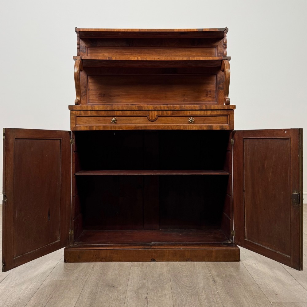 An antique Regency mahogany chiffonier featuring an upper two-tier shelf structure, a long drawer with star-shaped brass pulls, and a lower panelled double cupboard on a plinth base. View II