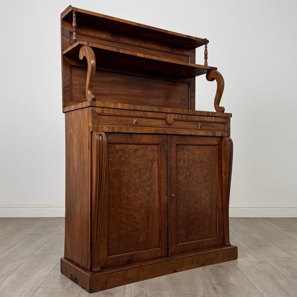 An antique Regency mahogany chiffonier featuring an upper two-tier shelf structure, a long drawer with star-shaped brass pulls, and a lower panelled double cupboard on a plinth base. View IX
