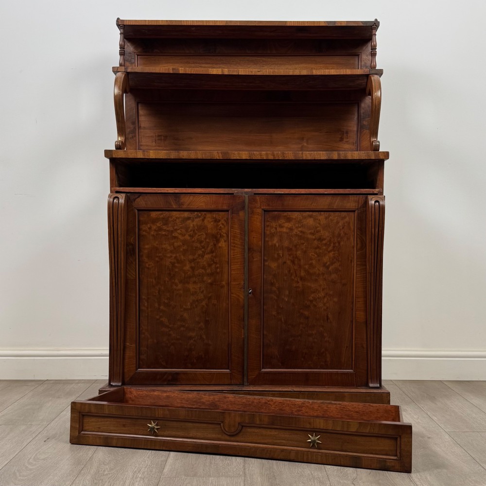 An antique Regency mahogany chiffonier featuring an upper two-tier shelf structure, a long drawer with star-shaped brass pulls, and a lower panelled double cupboard on a plinth base. View XI