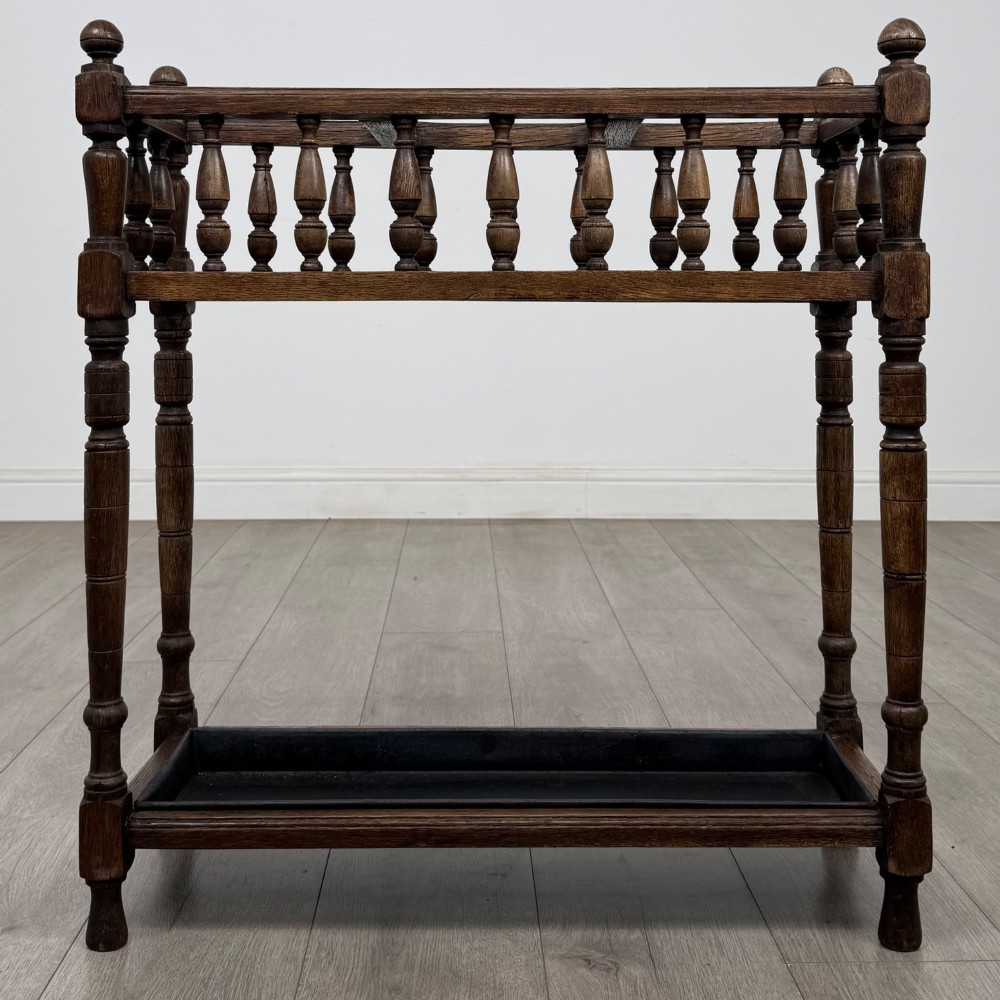 An Edwardian dark oak umbrella stand featuring turned corner posts, a top rail filled with turned spindles, and a lower drip tray.