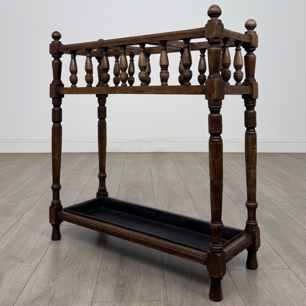 An Edwardian dark oak umbrella stand featuring turned corner posts, a top rail filled with turned spindles, and a lower drip tray. View II