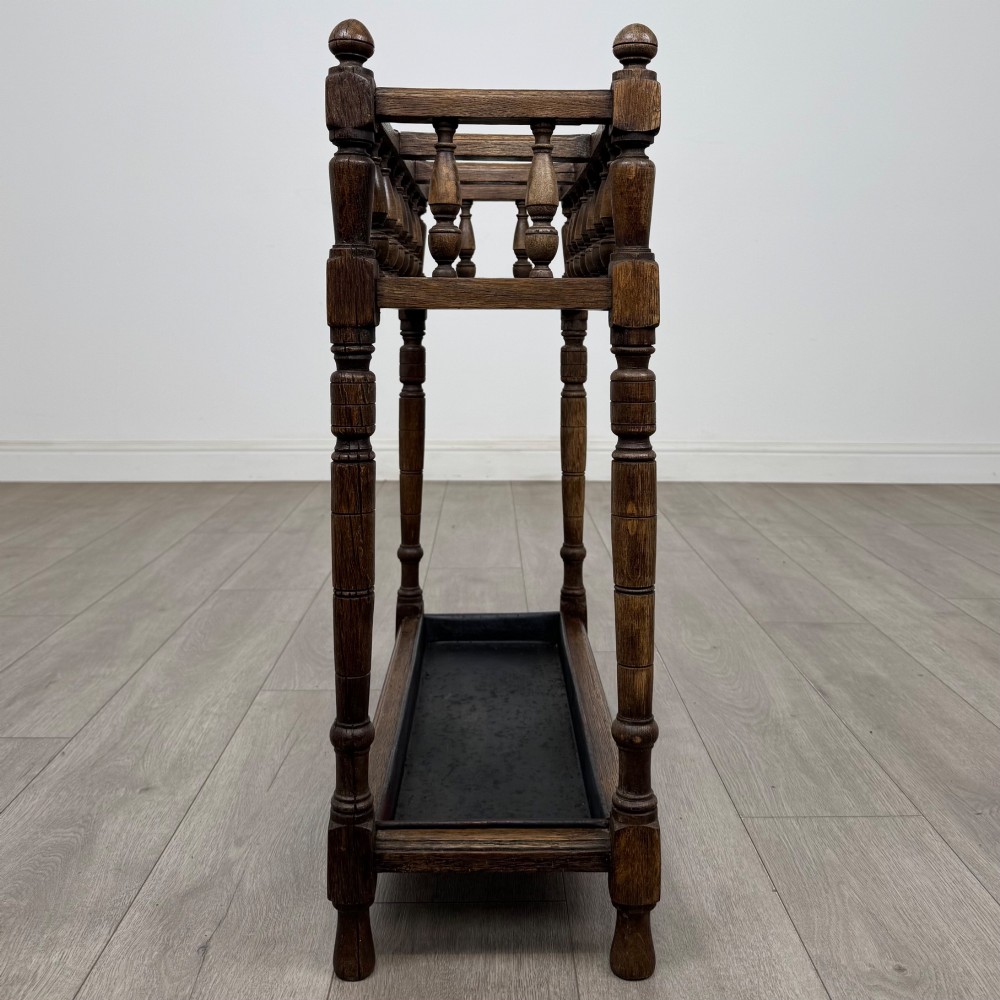 An Edwardian dark oak umbrella stand featuring turned corner posts, a top rail filled with turned spindles, and a lower drip tray. View III