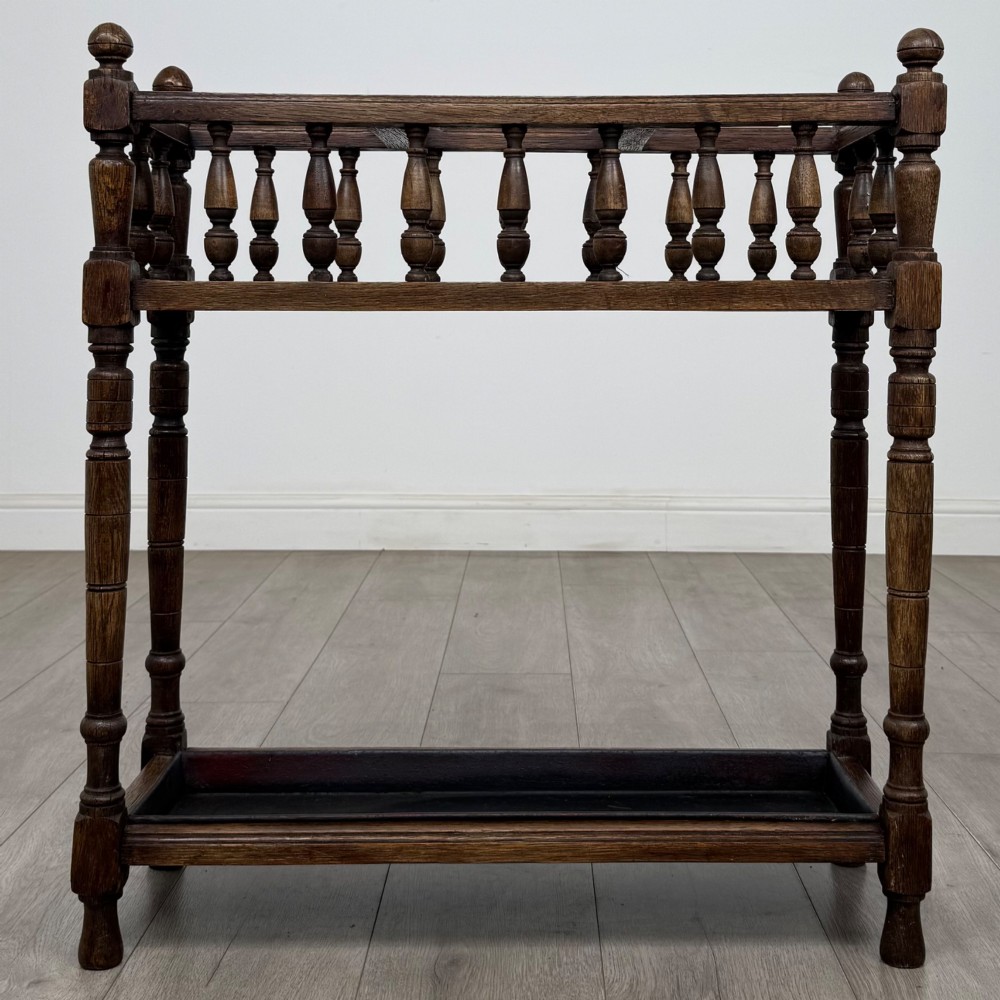 An Edwardian dark oak umbrella stand featuring turned corner posts, a top rail filled with turned spindles, and a lower drip tray. View V
