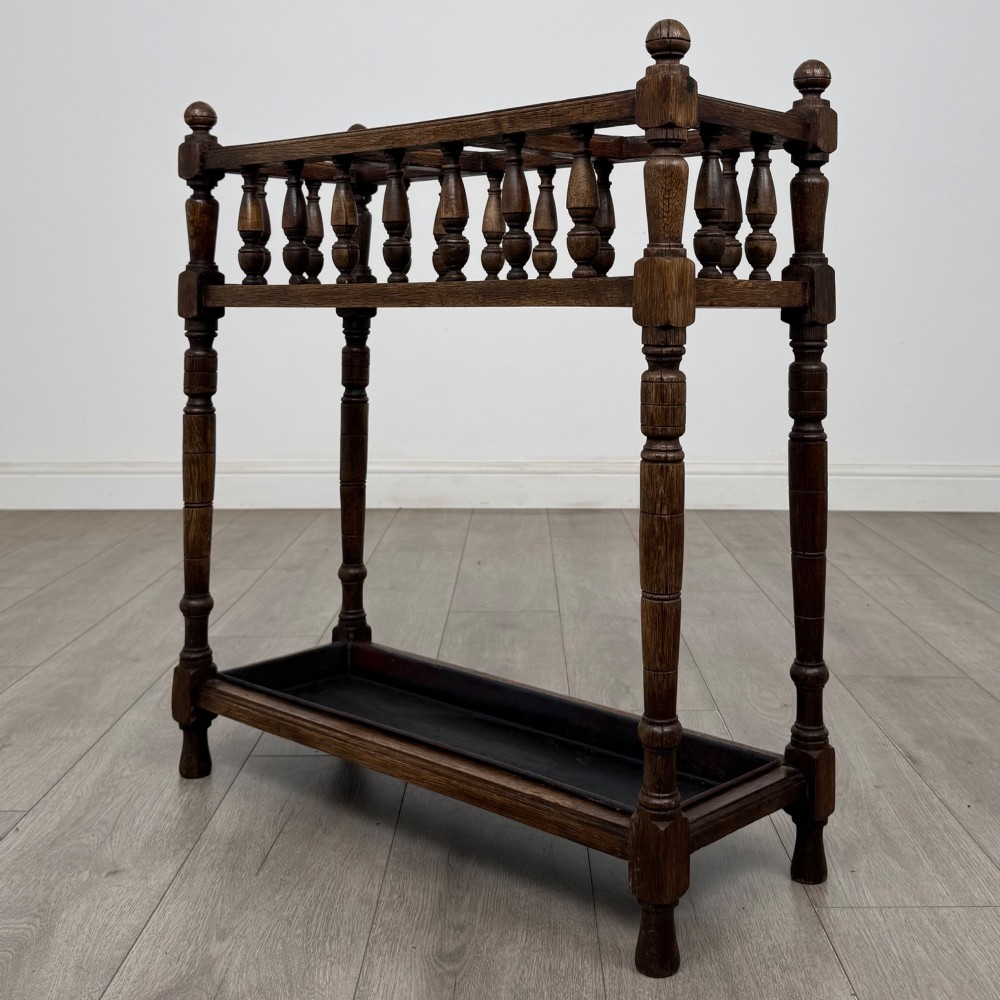 An Edwardian dark oak umbrella stand featuring turned corner posts, a top rail filled with turned spindles, and a lower drip tray. View VI
