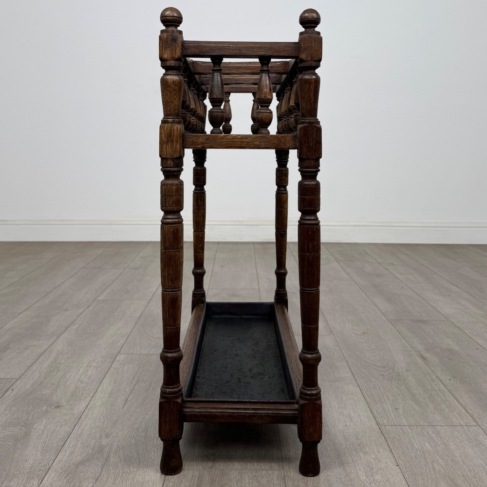 An Edwardian dark oak umbrella stand featuring turned corner posts, a top rail filled with turned spindles, and a lower drip tray. View VII