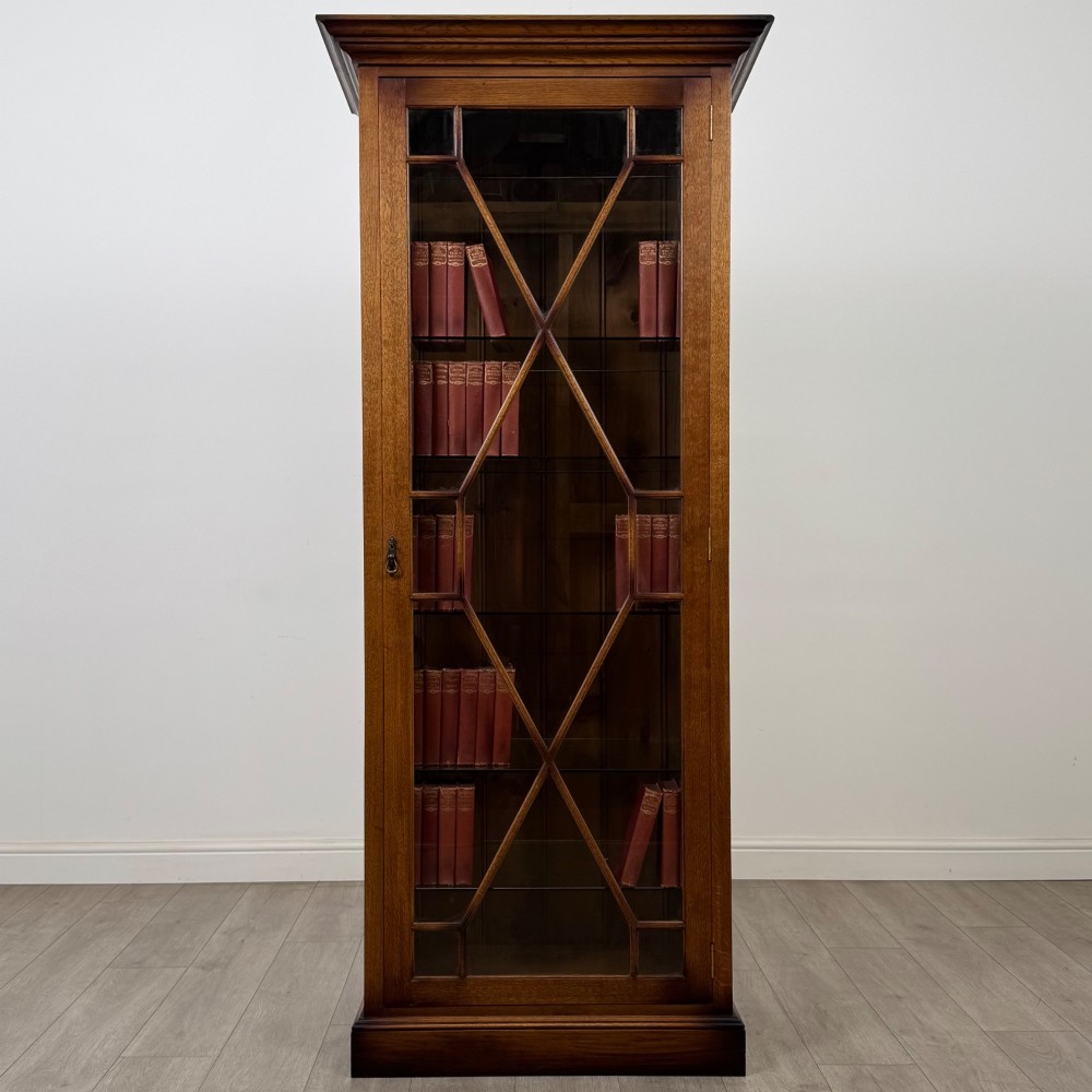 A tall 20th-century warm brown oak display cabinet featuring a single glass door with diamond-pattern astragal glazing bars, a moulded top cornice, and a solid plinth base.