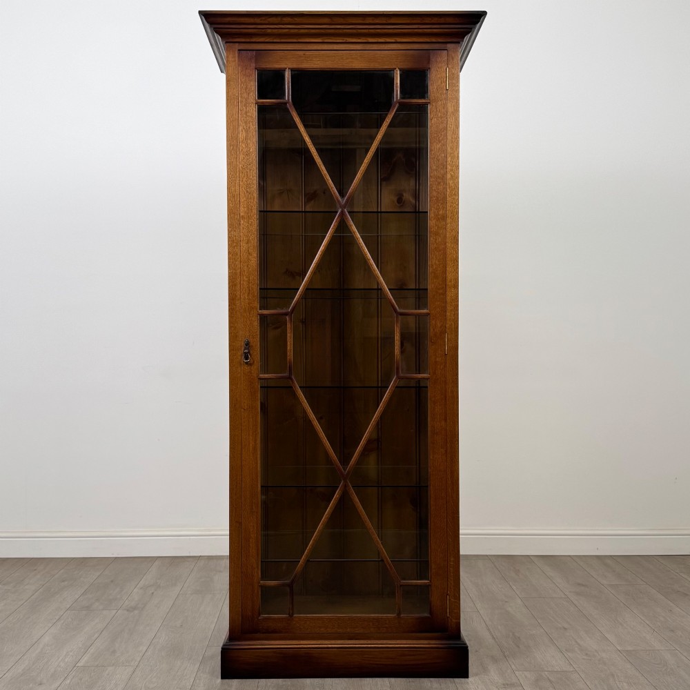 A tall 20th-century warm brown oak display cabinet featuring a single glass door with diamond-pattern astragal glazing bars, a moulded top cornice, and a solid plinth base. View II