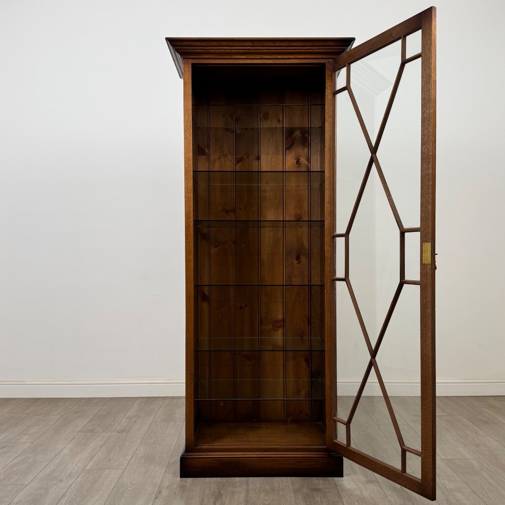 A tall 20th-century warm brown oak display cabinet featuring a single glass door with diamond-pattern astragal glazing bars, a moulded top cornice, and a solid plinth base. View III