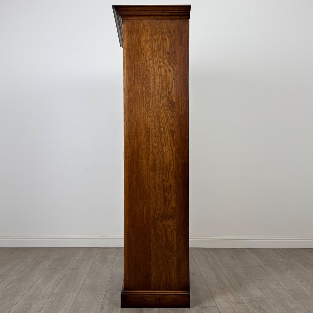 A tall 20th-century warm brown oak display cabinet featuring a single glass door with diamond-pattern astragal glazing bars, a moulded top cornice, and a solid plinth base. View V
