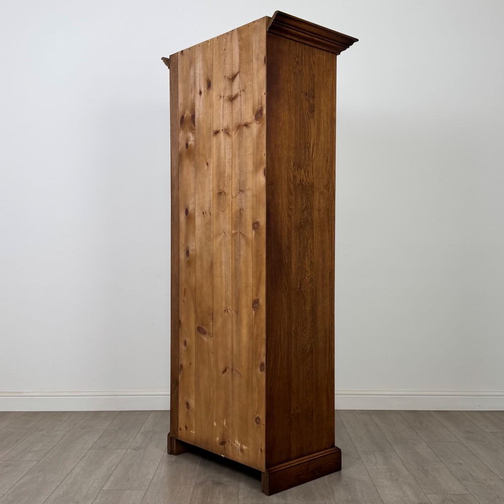A tall 20th-century warm brown oak display cabinet featuring a single glass door with diamond-pattern astragal glazing bars, a moulded top cornice, and a solid plinth base. View VIII