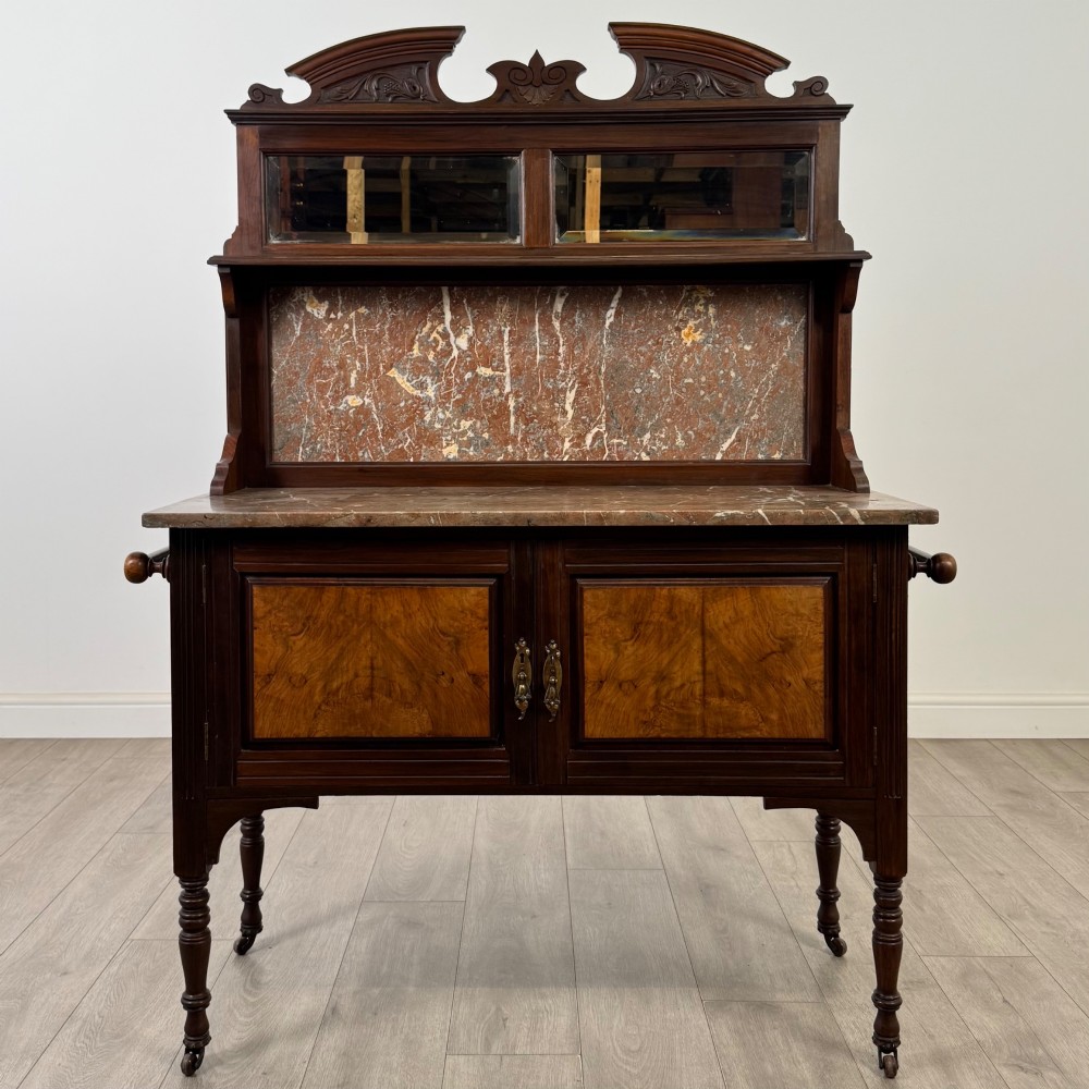 An Edwardian walnut washstand featuring a red marble splashback, mirror gallery top, double cupboard doors with burr walnut panels, and turned legs on castors.