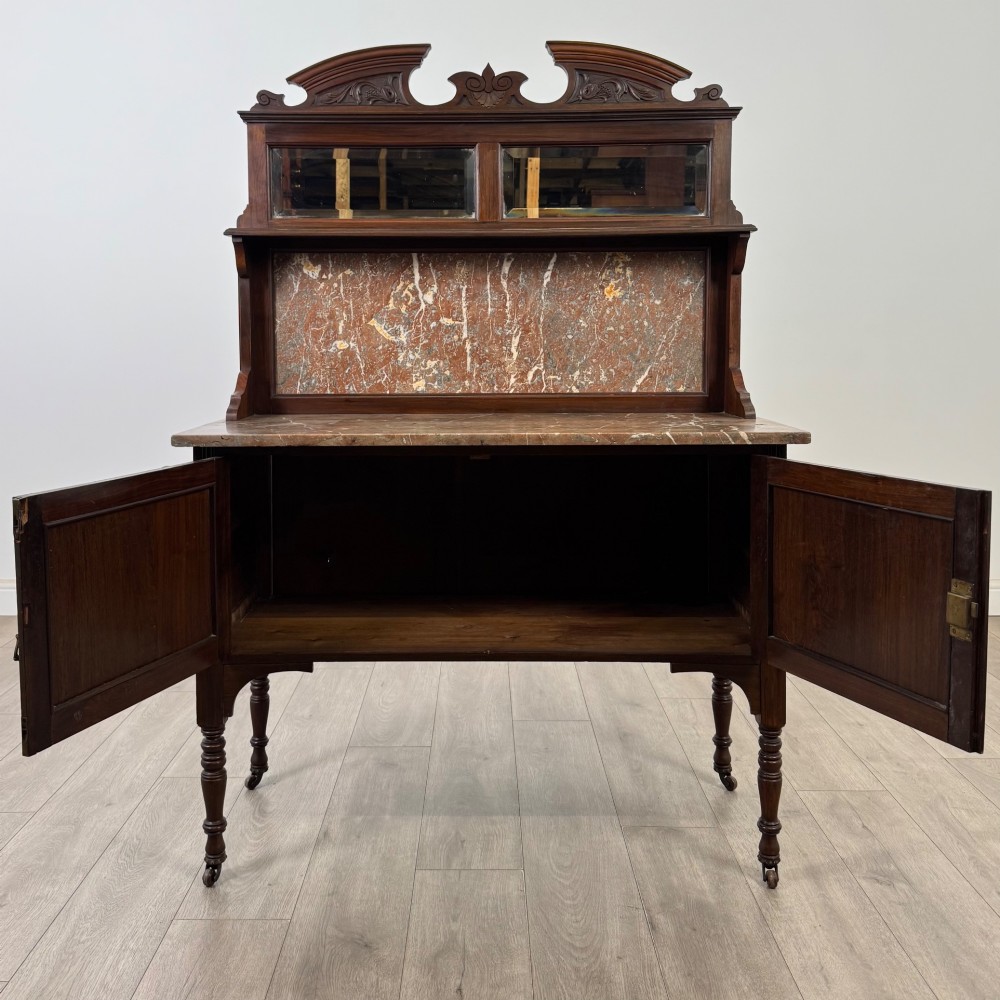 An Edwardian walnut washstand featuring a red marble splashback, mirror gallery top, double cupboard doors with burr walnut panels, and turned legs on castors. View II
