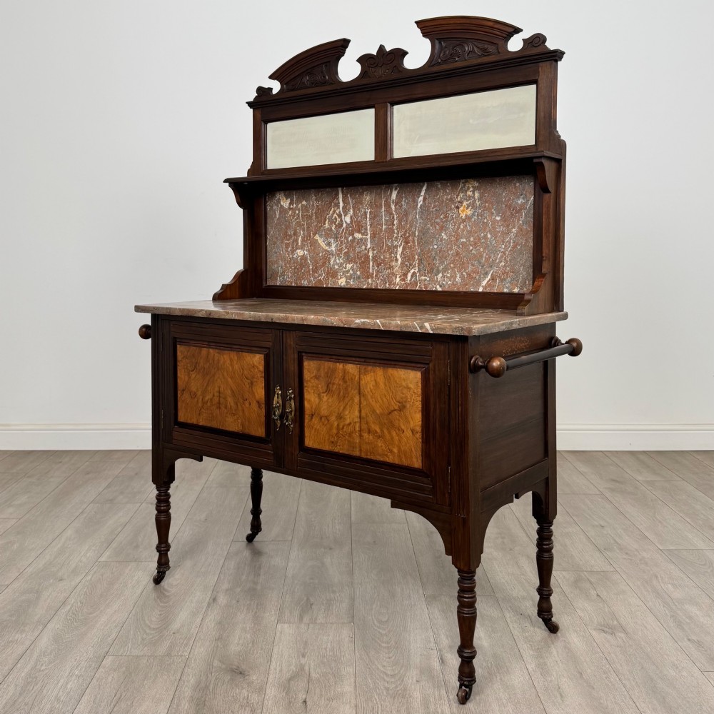 An Edwardian walnut washstand featuring a red marble splashback, mirror gallery top, double cupboard doors with burr walnut panels, and turned legs on castors. View III