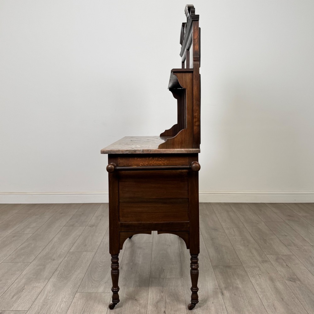 An Edwardian walnut washstand featuring a red marble splashback, mirror gallery top, double cupboard doors with burr walnut panels, and turned legs on castors. View IV