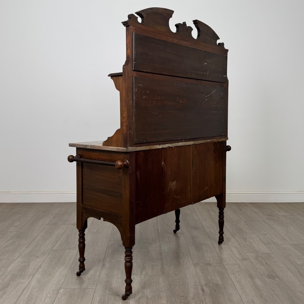 An Edwardian walnut washstand featuring a red marble splashback, mirror gallery top, double cupboard doors with burr walnut panels, and turned legs on castors. View V
