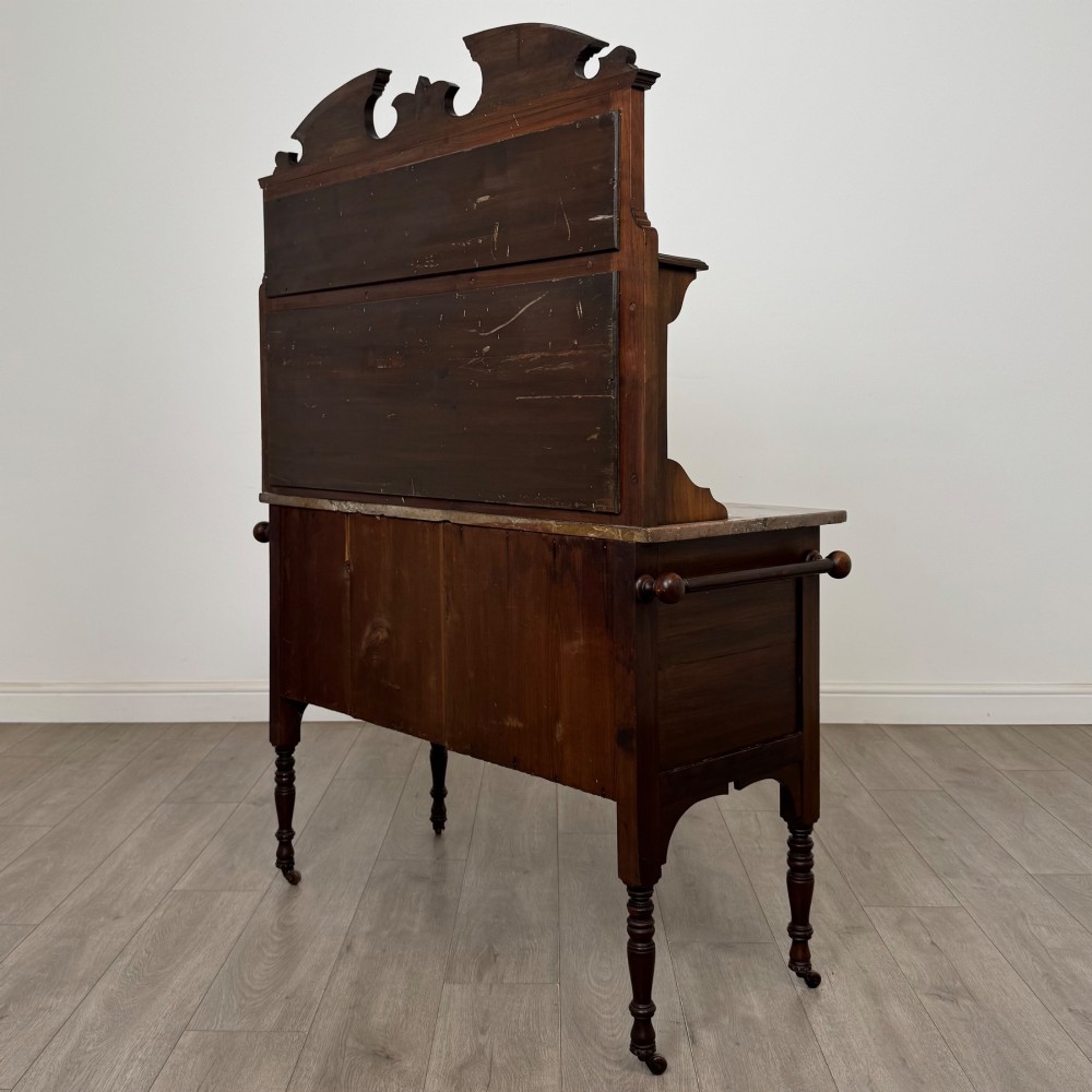 An Edwardian walnut washstand featuring a red marble splashback, mirror gallery top, double cupboard doors with burr walnut panels, and turned legs on castors. View VII