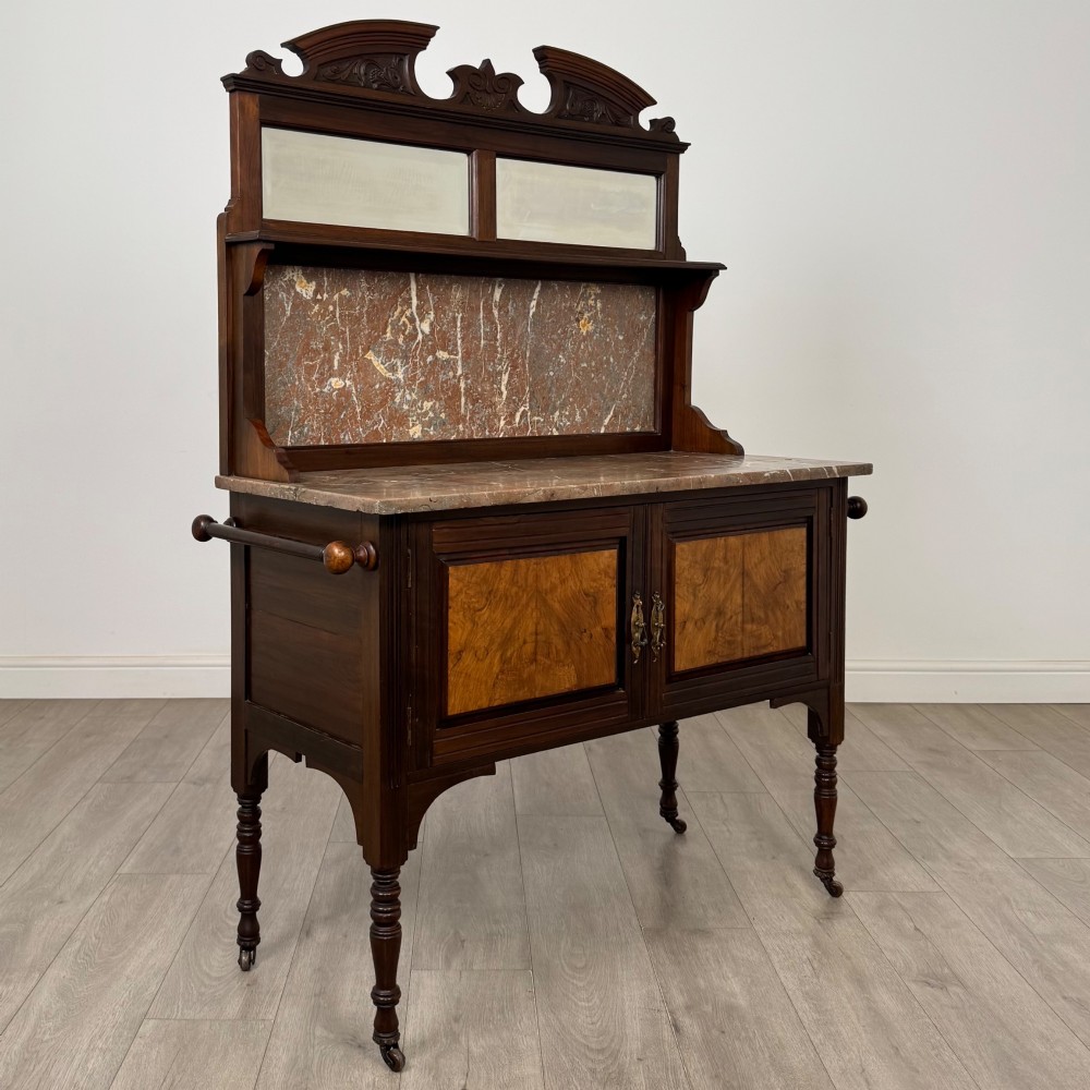 An Edwardian walnut washstand featuring a red marble splashback, mirror gallery top, double cupboard doors with burr walnut panels, and turned legs on castors. View IX
