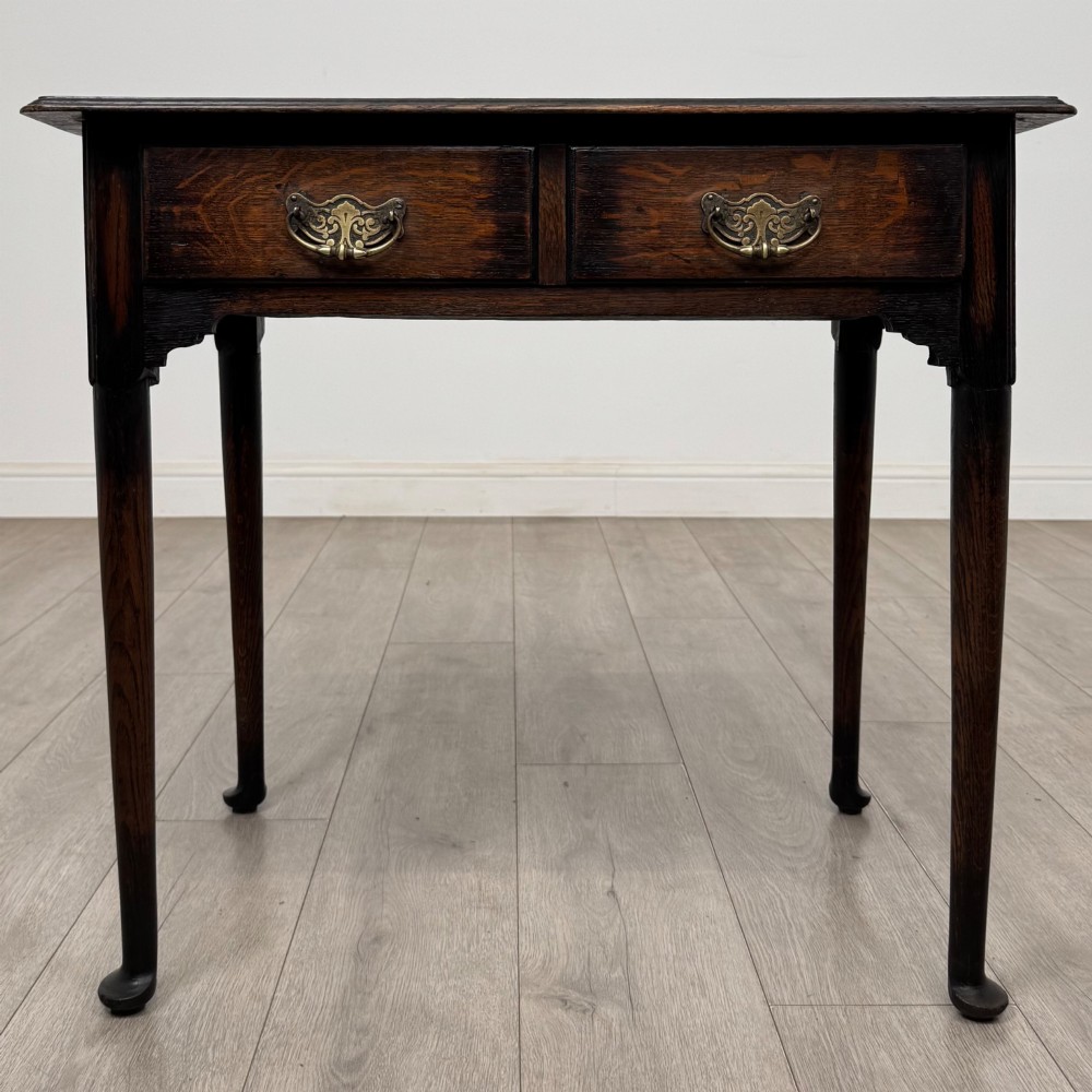 A dark oak Edwardian side table featuring two drawers with brass handles and tapered legs ending in pad feet.