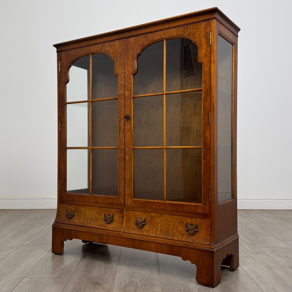 A 20th-century burr walnut display cabinet featuring two glazed doors with arched detail above two drawers on bracket feet. View III
