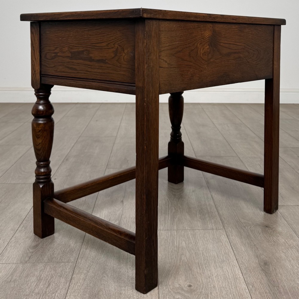 A dark oak side table featuring a single drawer with geometric mitred moulding, turned wooden knobs, a shaped lower apron, and baluster turned legs linked by low stretchers. View IV