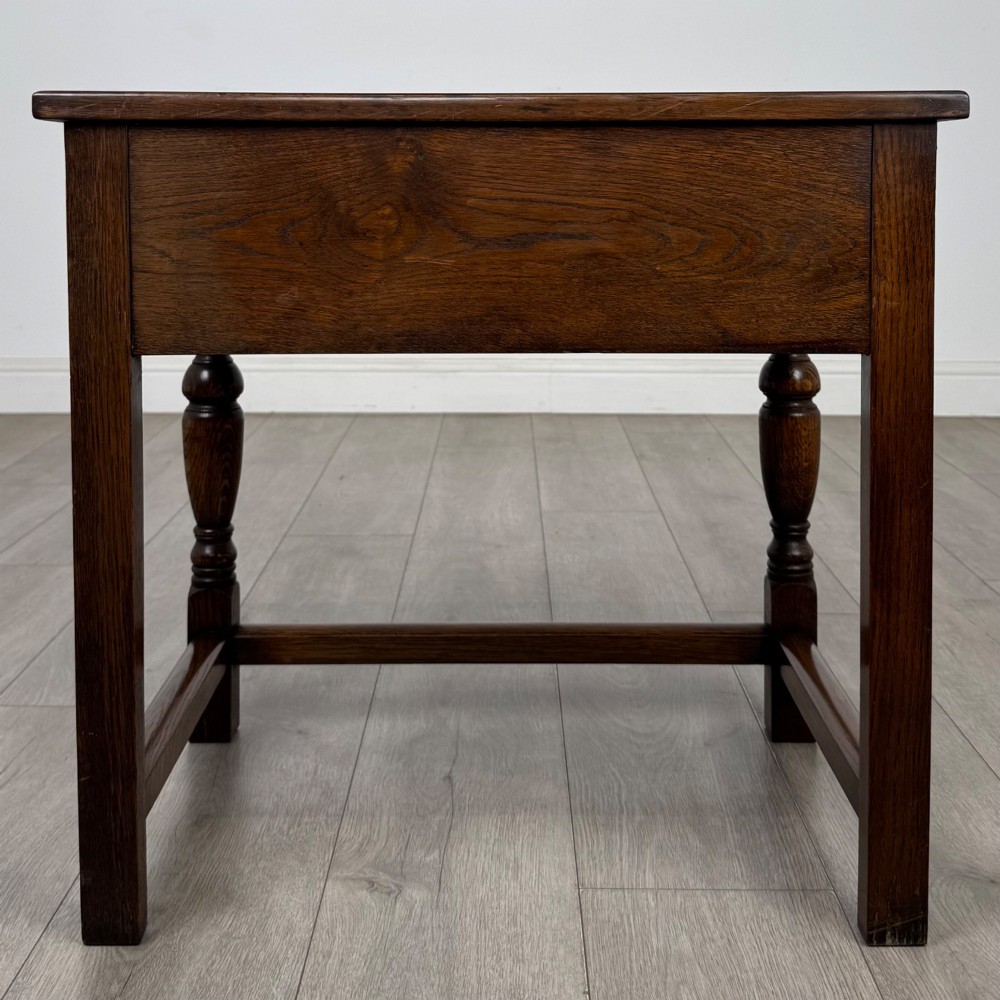 A dark oak side table featuring a single drawer with geometric mitred moulding, turned wooden knobs, a shaped lower apron, and baluster turned legs linked by low stretchers. View V