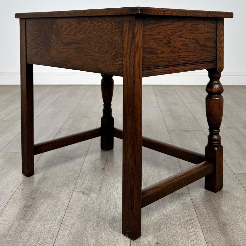 A dark oak side table featuring a single drawer with geometric mitred moulding, turned wooden knobs, a shaped lower apron, and baluster turned legs linked by low stretchers. View VI