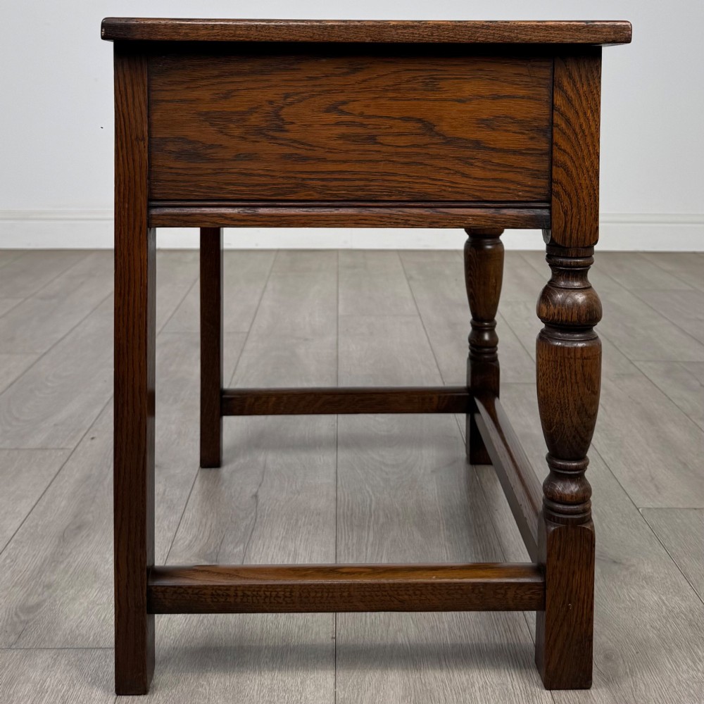 A dark oak side table featuring a single drawer with geometric mitred moulding, turned wooden knobs, a shaped lower apron, and baluster turned legs linked by low stretchers. View VII