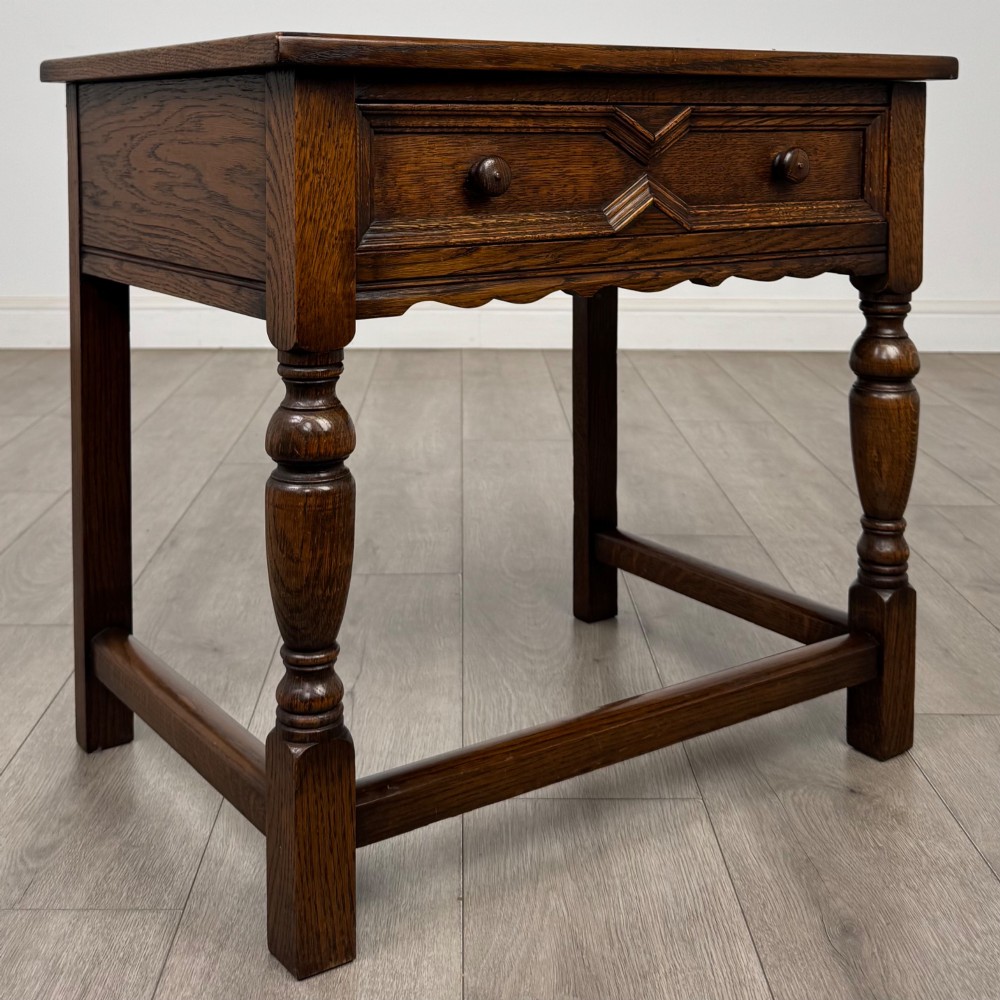 A dark oak side table featuring a single drawer with geometric mitred moulding, turned wooden knobs, a shaped lower apron, and baluster turned legs linked by low stretchers. View VIII