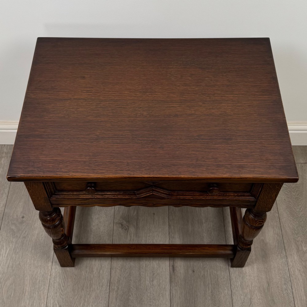 A dark oak side table featuring a single drawer with geometric mitred moulding, turned wooden knobs, a shaped lower apron, and baluster turned legs linked by low stretchers. View IX