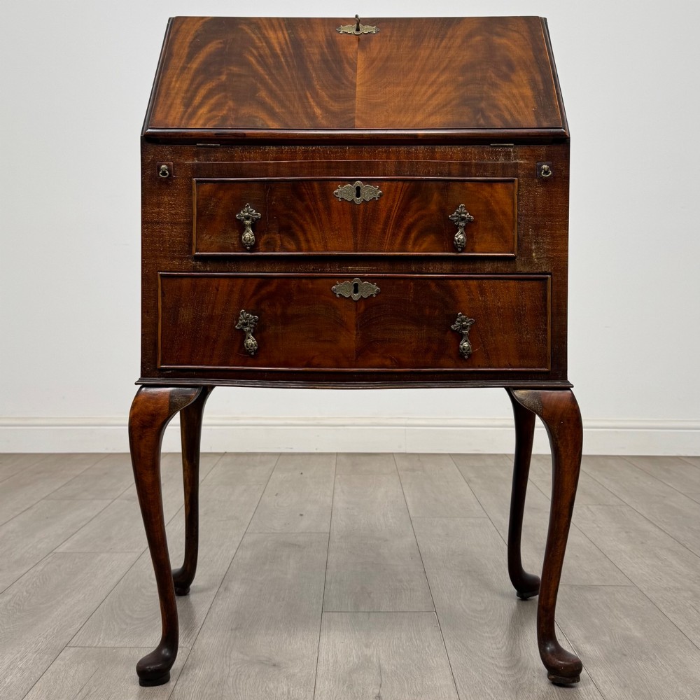 An Edwardian mahogany writing bureau featuring a sloped drop-front lid above two drawers, supported by four slender cabriole legs.