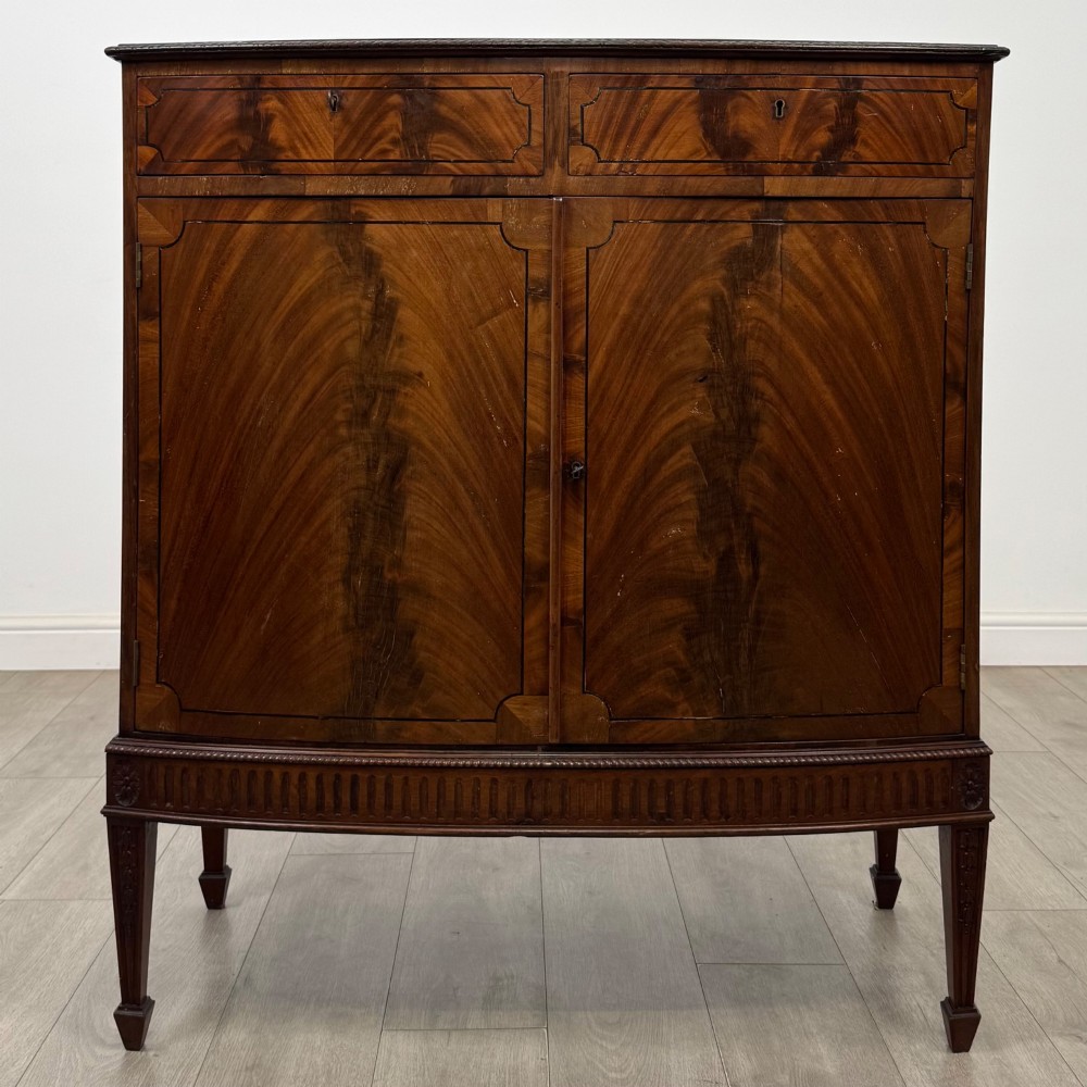 An 18th-century Georgian mahogany cupboard featuring flame veneer panelled doors, upper drawer section, a fluted apron, and tapered legs.
