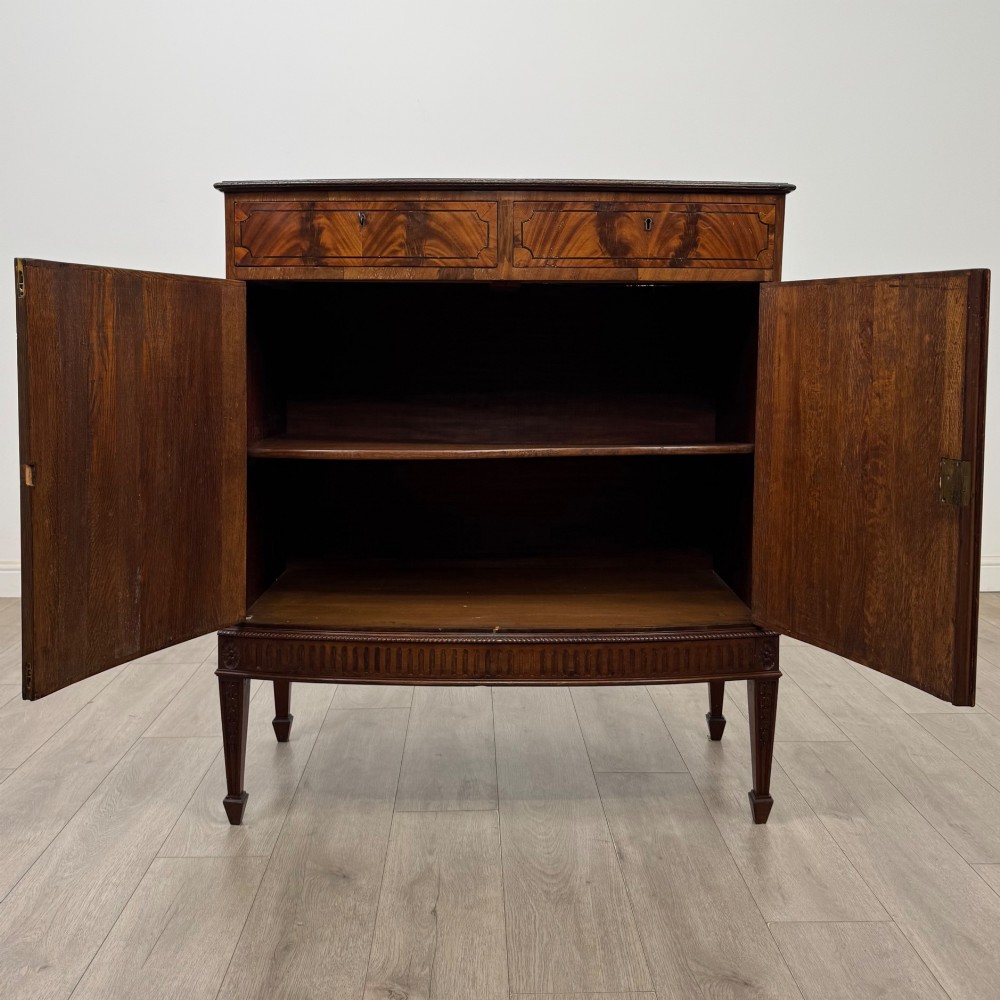 An 18th-century Georgian mahogany cupboard featuring flame veneer panelled doors, upper drawer section, a fluted apron, and tapered legs. View II