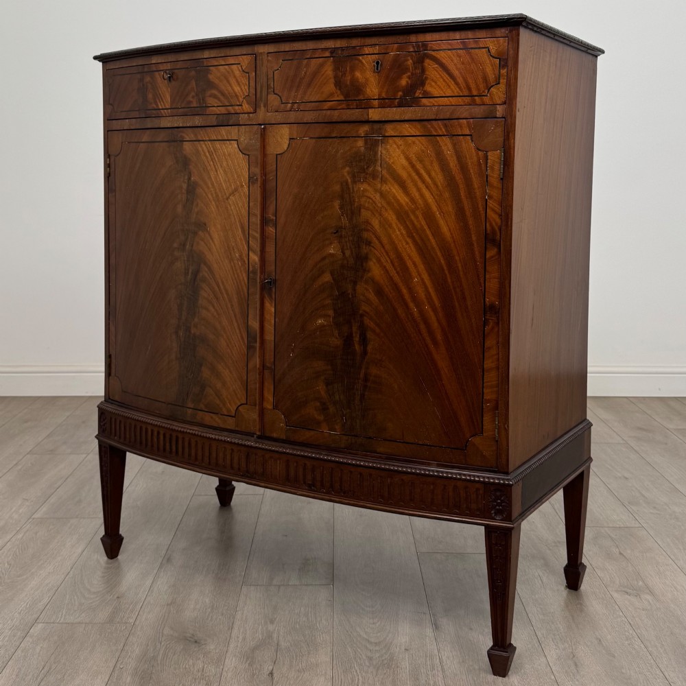 An 18th-century Georgian mahogany cupboard featuring flame veneer panelled doors, upper drawer section, a fluted apron, and tapered legs. View III