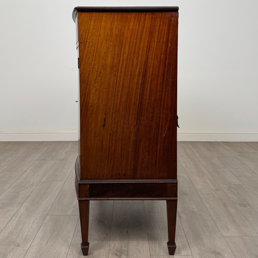 An 18th-century Georgian mahogany cupboard featuring flame veneer panelled doors, upper drawer section, a fluted apron, and tapered legs. View IV