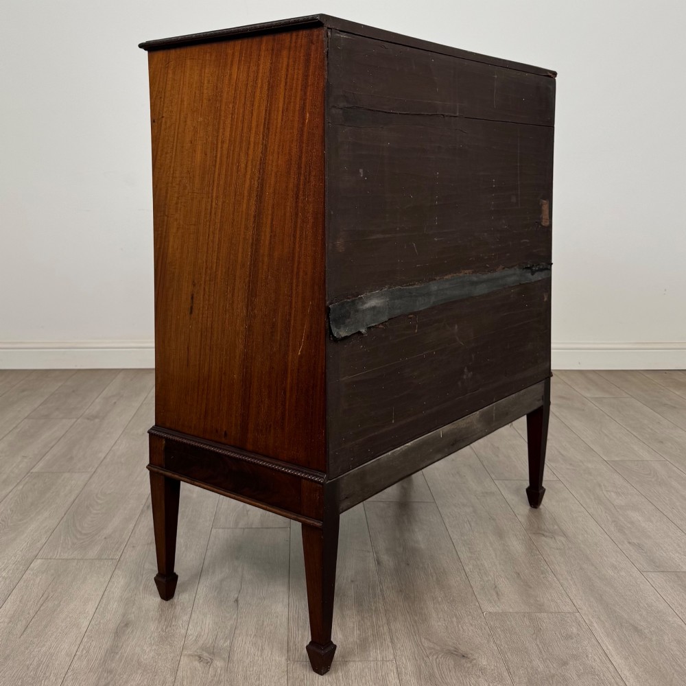 An 18th-century Georgian mahogany cupboard featuring flame veneer panelled doors, upper drawer section, a fluted apron, and tapered legs. View V