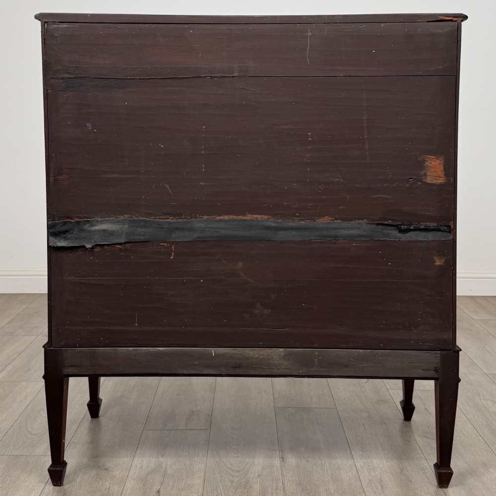 An 18th-century Georgian mahogany cupboard featuring flame veneer panelled doors, upper drawer section, a fluted apron, and tapered legs. View VI