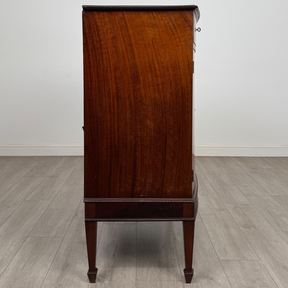 An 18th-century Georgian mahogany cupboard featuring flame veneer panelled doors, upper drawer section, a fluted apron, and tapered legs. View VIII