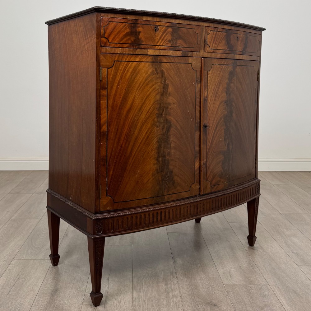 An 18th-century Georgian mahogany cupboard featuring flame veneer panelled doors, upper drawer section, a fluted apron, and tapered legs. View IX